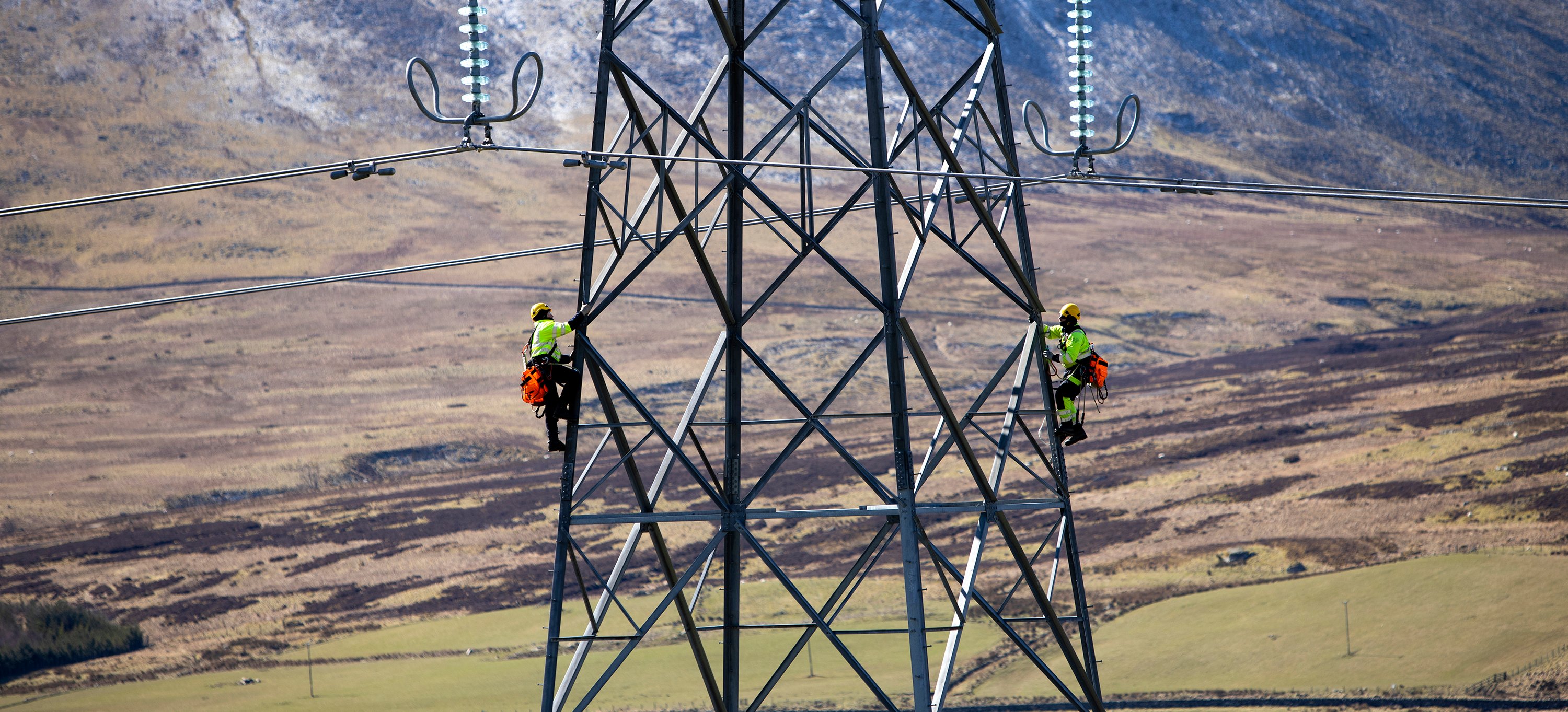 Two engineers climb a transmission tower