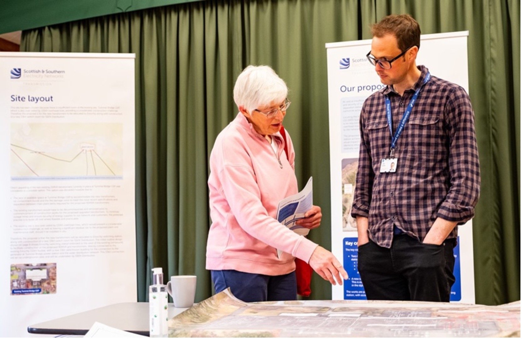 An SSEN Transmission employee and a member of the public examining maps on a table. Project posters are visible behind them.