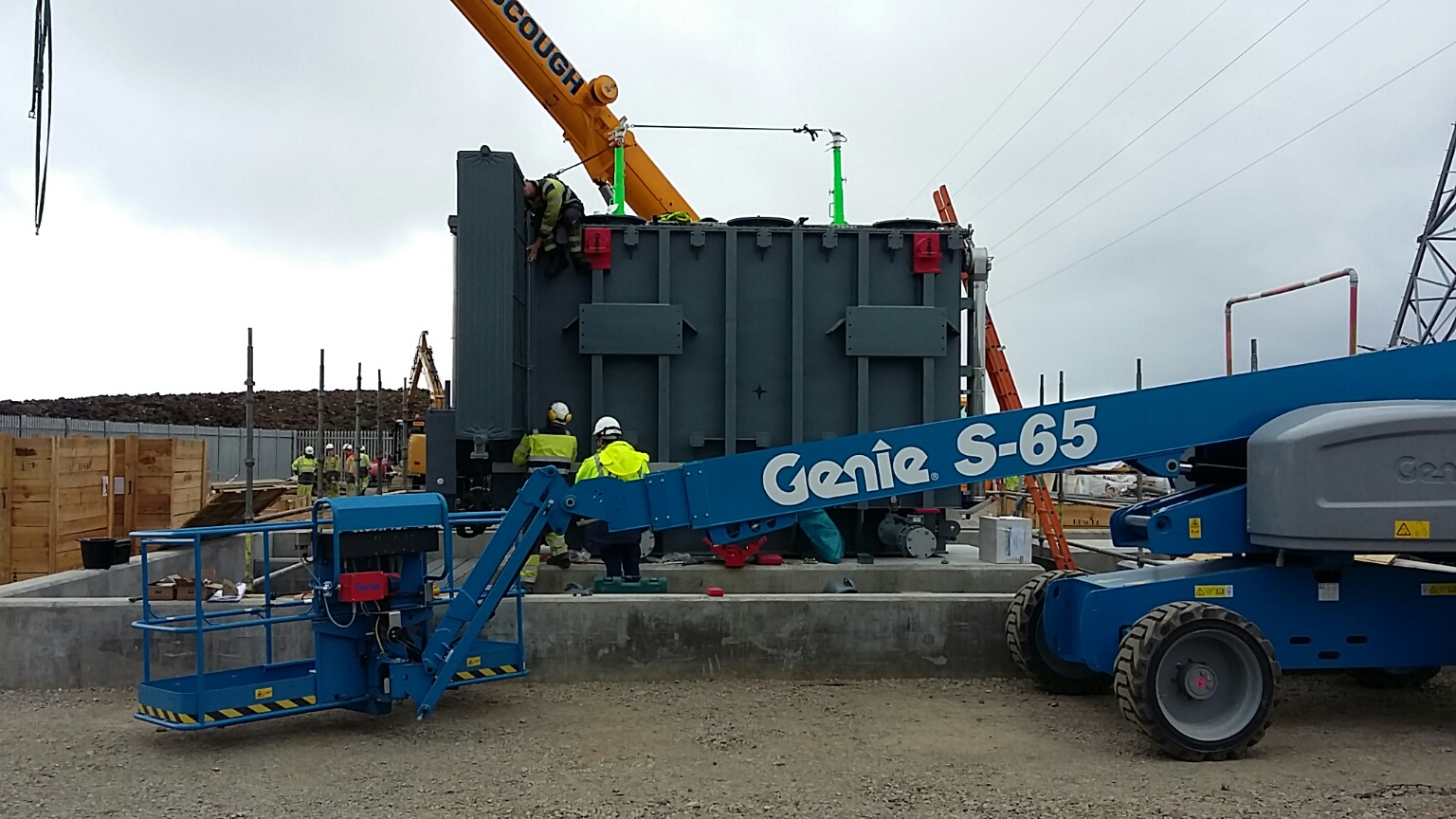 A large section of substation infrastructure mounted on a concrete platform surrounded by construction vehicles and contractors in PPE.