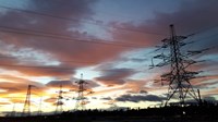 Several different kinds of metal transmission towers, outlined against a sunset.