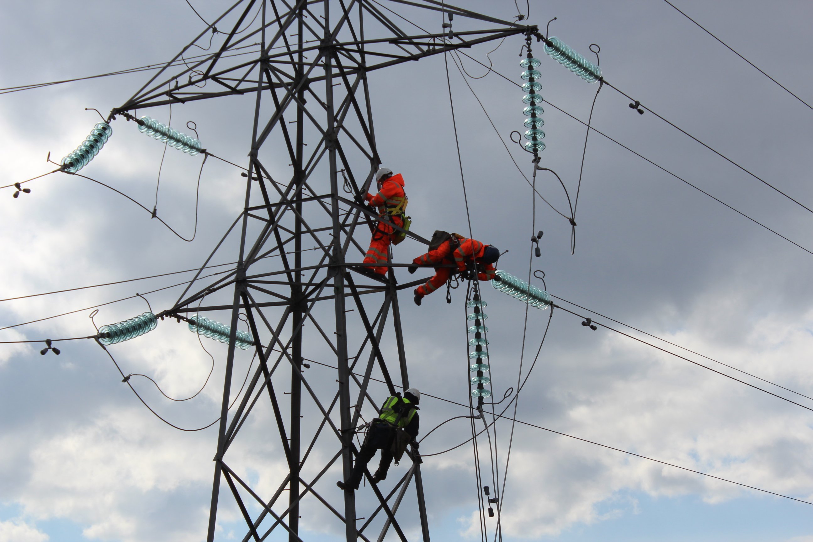 Contractors in PPE atop a metal transmission tower.