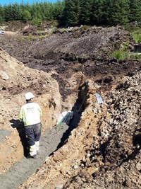 A contractor in PPE in an excavated trench. Black and green cylinders are present in the trench.