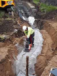 A contractor in PPE with machinery in an excavated trench.