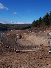 A rectangular excavated area surrounded by temporary metal barriers.