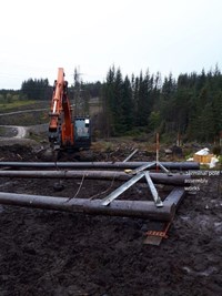 A woodpole trident transmission tower laying on the ground next to a construction vehicle.