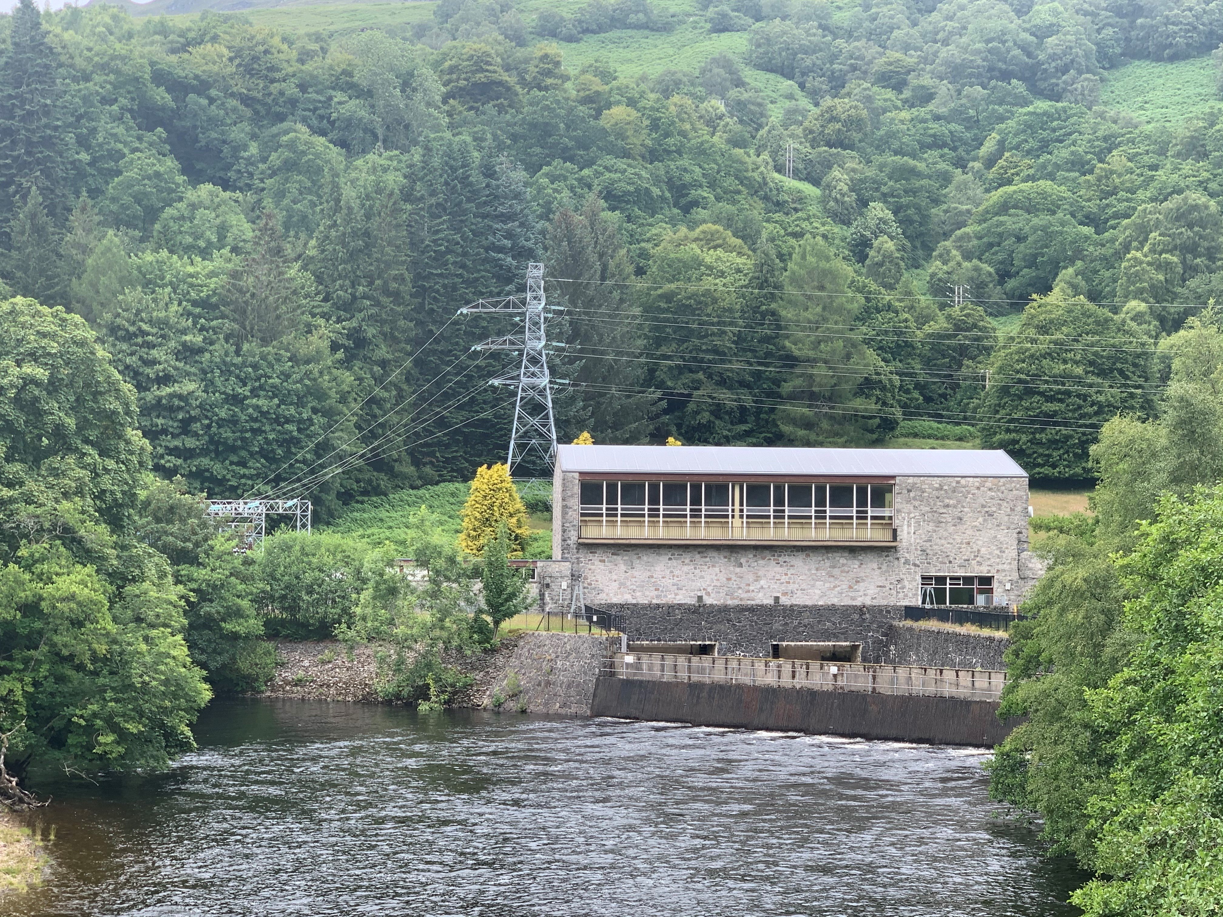 A stone building, an overhead line leads into a courtyard obscured by trees.