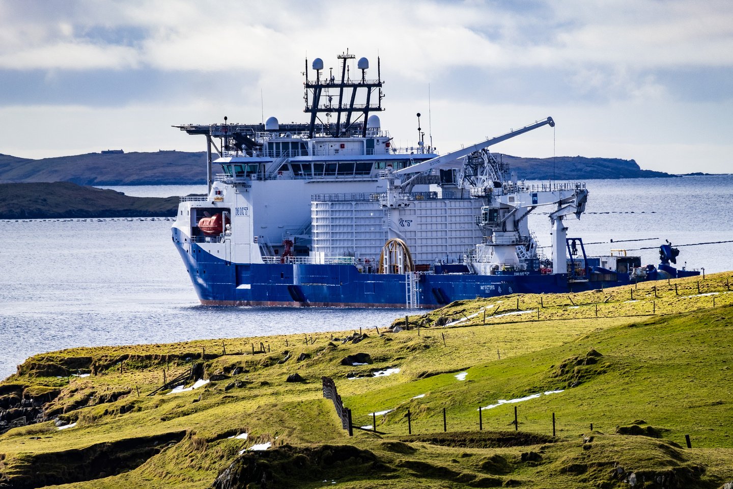 A large ship near a grassy shore.