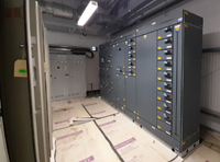 A large dark-grey metal cuboid along the wall of a florescent-lit room with cardboard covering the floor.