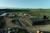 A construction site with two large green metal walled buildings.