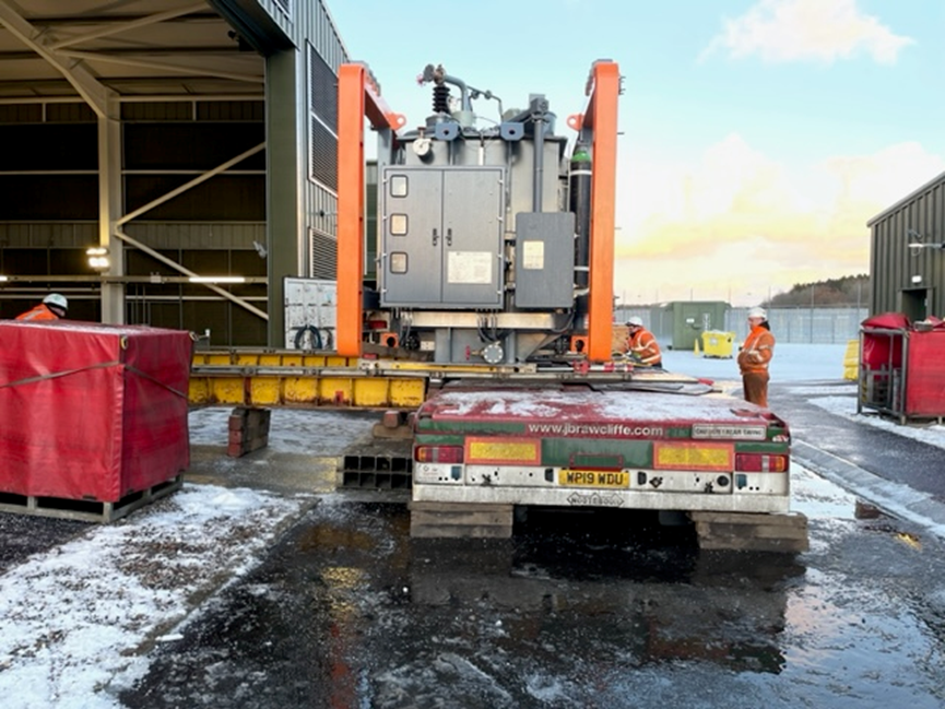 A large grey section of substation infrastructure atop a flatbed trailer.