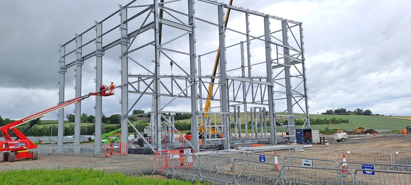 A metal frame work surrounded by  construction vehicles