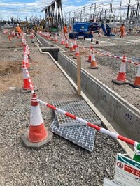 A concrete lined trench surrounded by traffic cones. In the background are several construction vehicles and substation infrastructure.