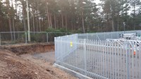 A metal fence line separating substation infrastructure from a wooded area.