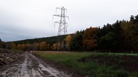 Disconnected metal transmission tower next to a dirt access road.