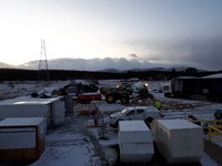 A snow covered construction site populated by construction vehicles, a tractor and a heavy goods vehicle.