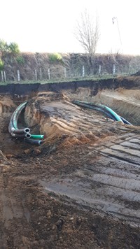 Two excavated areas with black and green cylinders exposed within.