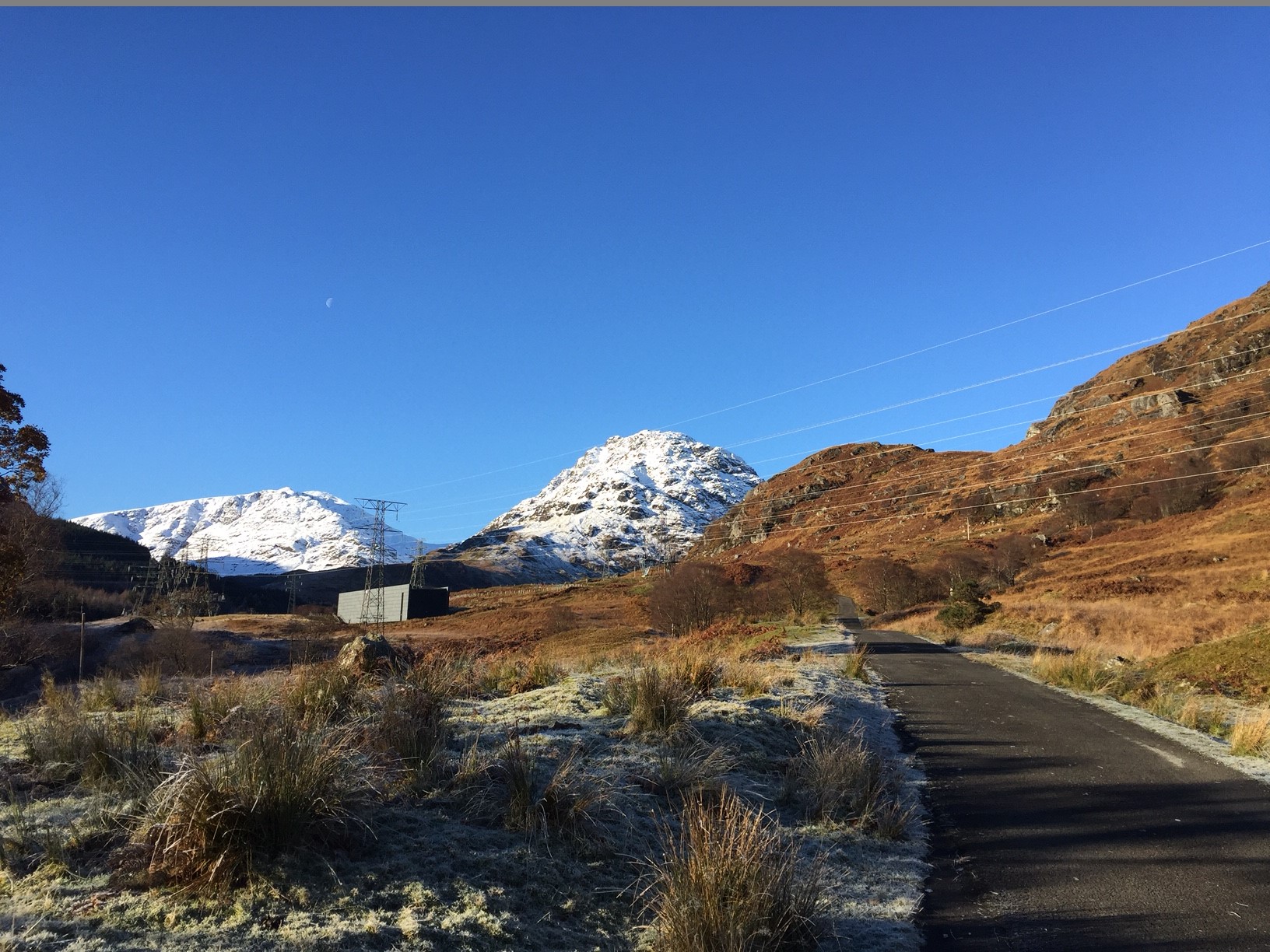 A road leading to snow covered hills, metal transmission towers are present to one side.